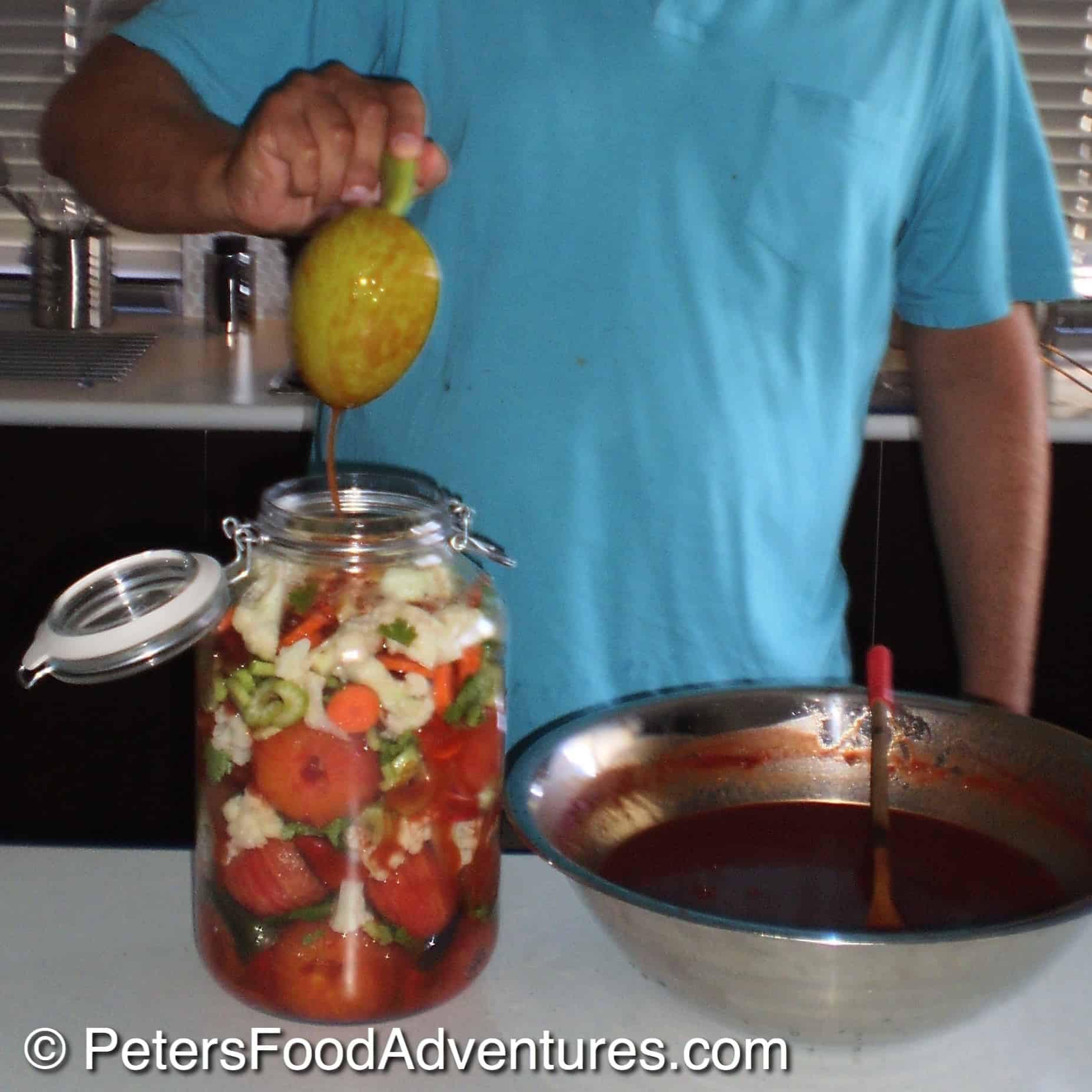 pouring hot brine over tomatoes and vegetables in a jar