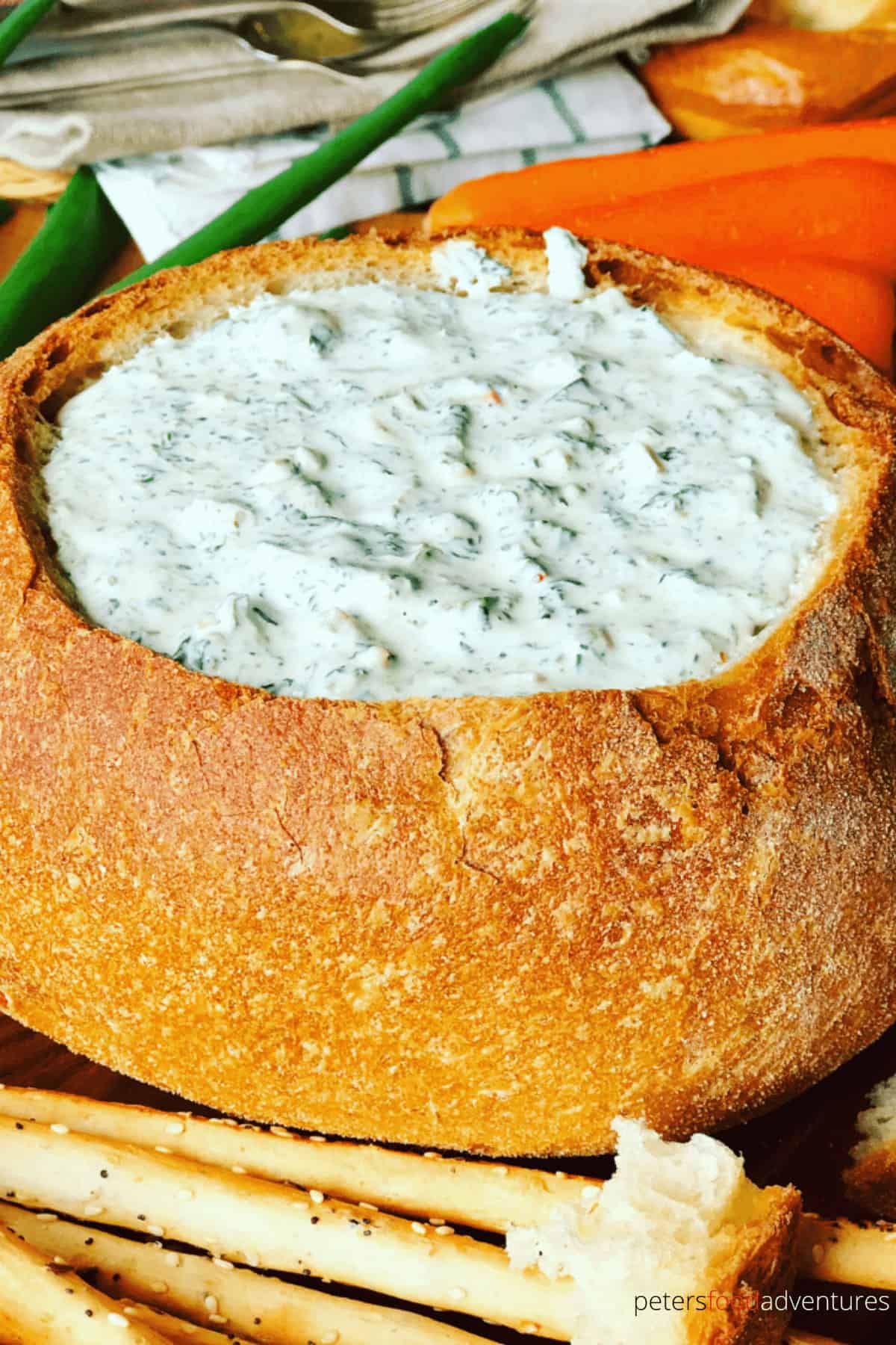 spinach dip in a bread bowl beside grissini sticks