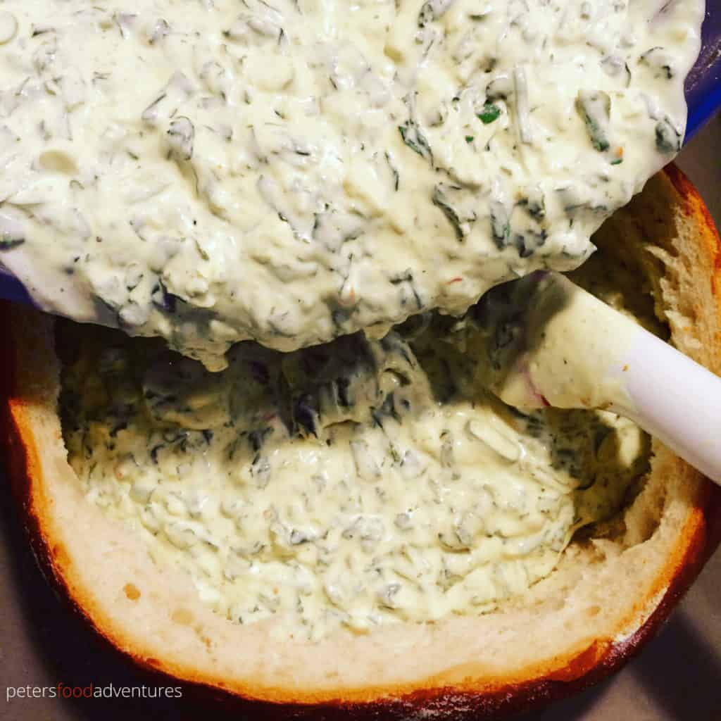 pouring spinach dip into hollowed out bread bowl
