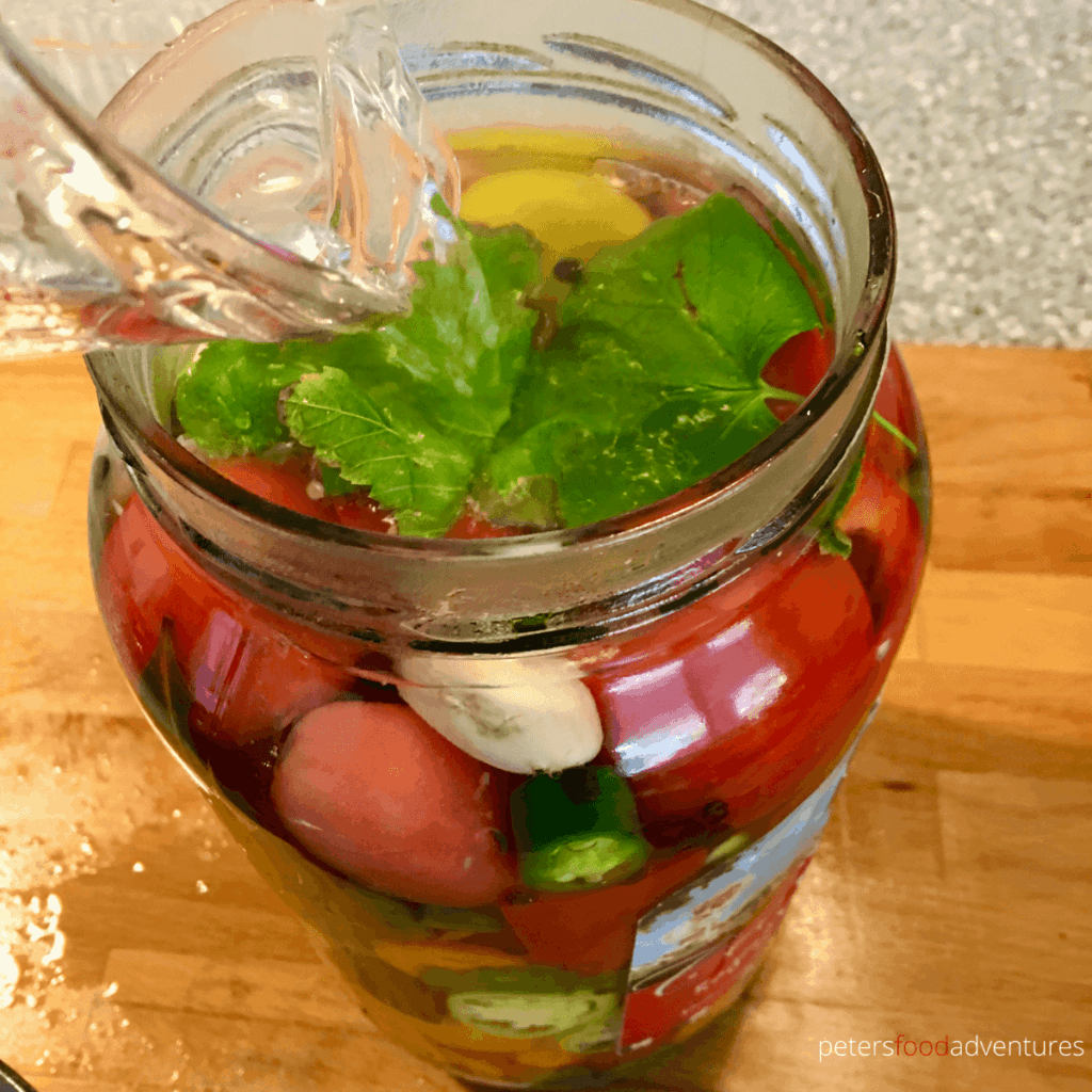 pouring hot vinegar brine to a jar of tomatoes and vegetables