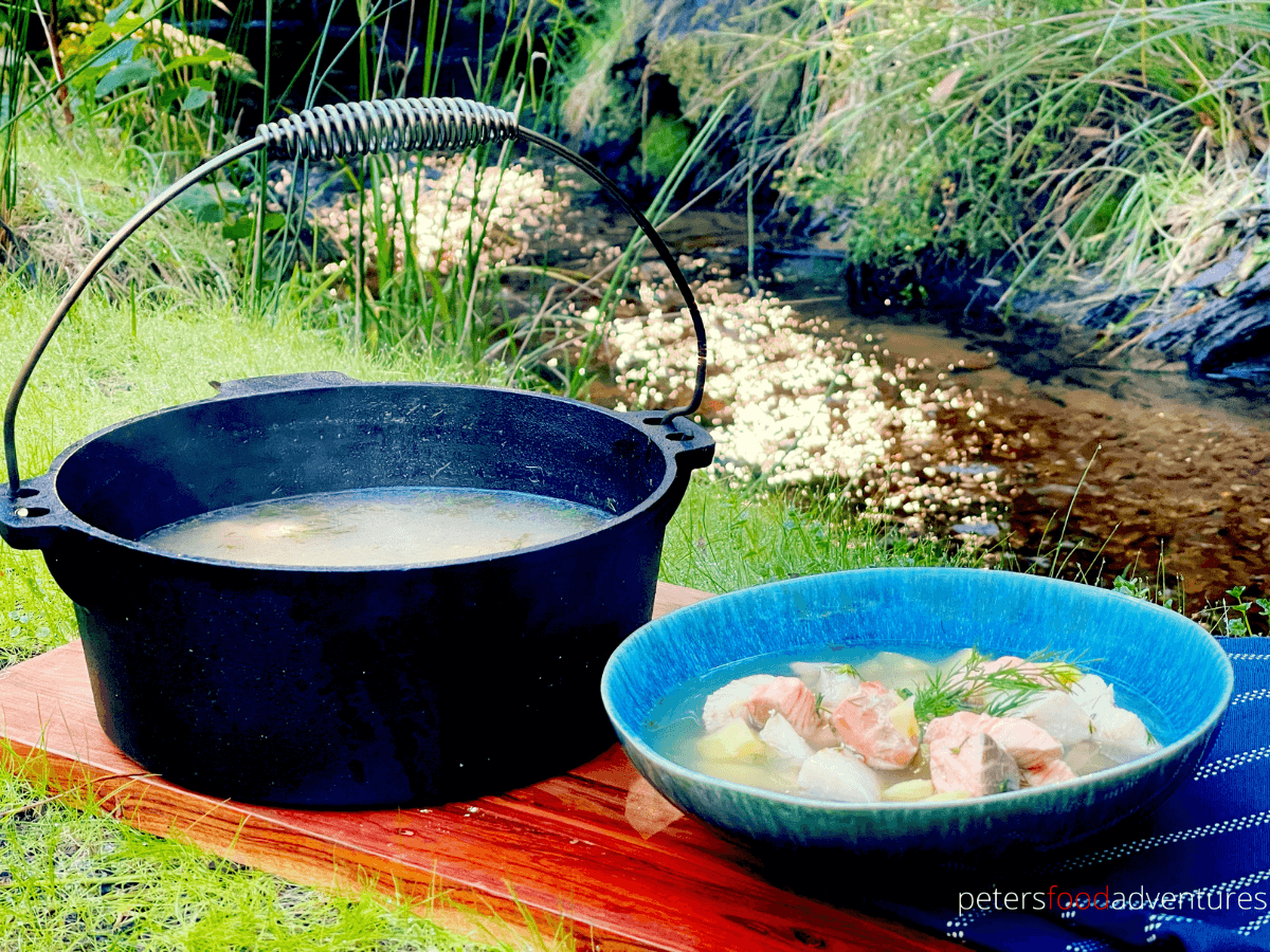 Rustic Russian Fish Head Soup, Ukha (Уха), in a bowl beside a cast iron pot it was cooked in, beside a creek
