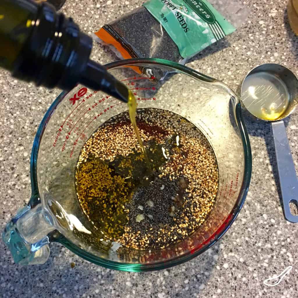 pouring olive oil into a homemade poppyseed dressing