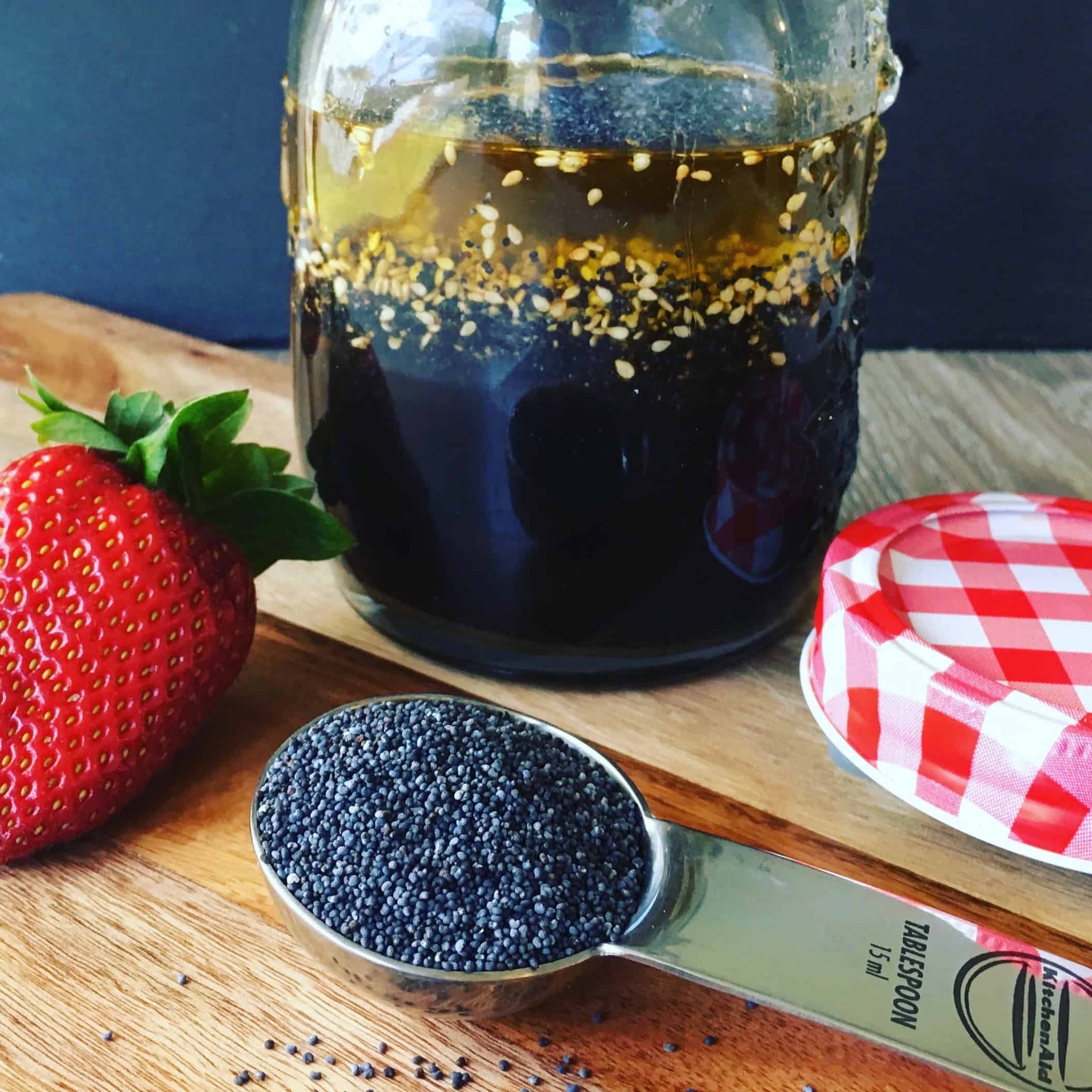 Jar of Poppy Seed Salad Dressing with a spoon of Poppy Seeds and Strawberries