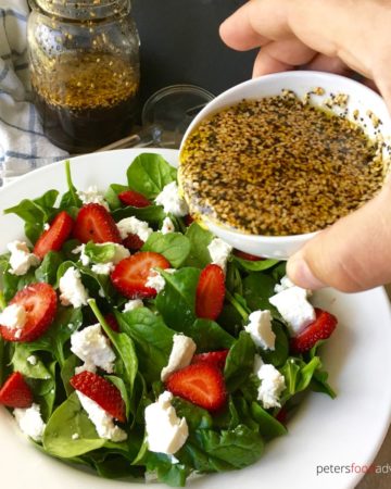 Pouring poppyseed dressing over strawberry spinach salad