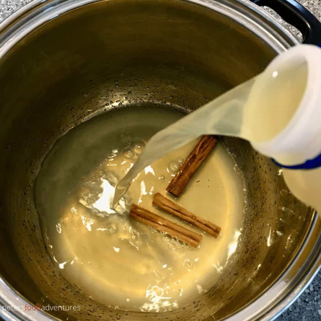 pouring apple juice into a pot with cinnamon quills
