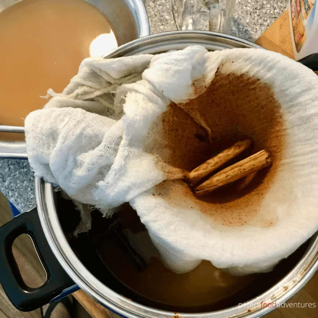 straining the spices from homemade hot apple cider in a cheesecloth