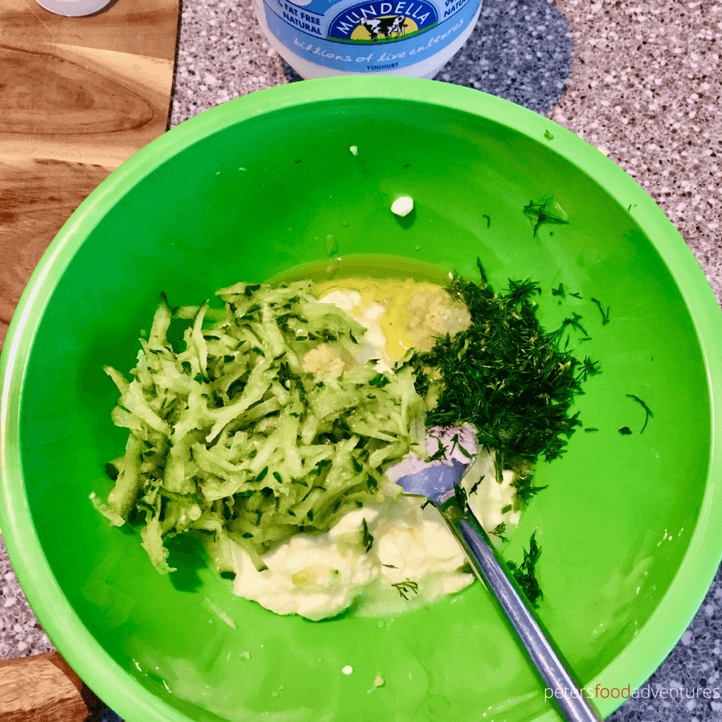 making tzatziki by mixing grated cucumber, dill and yogurt together