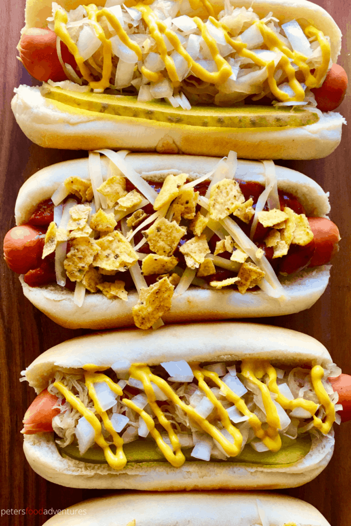 several hot dogs all in a row, with different toppings like chili and sauerkraut