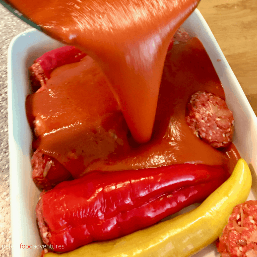 pouring tomato sauce on stuffed peppers