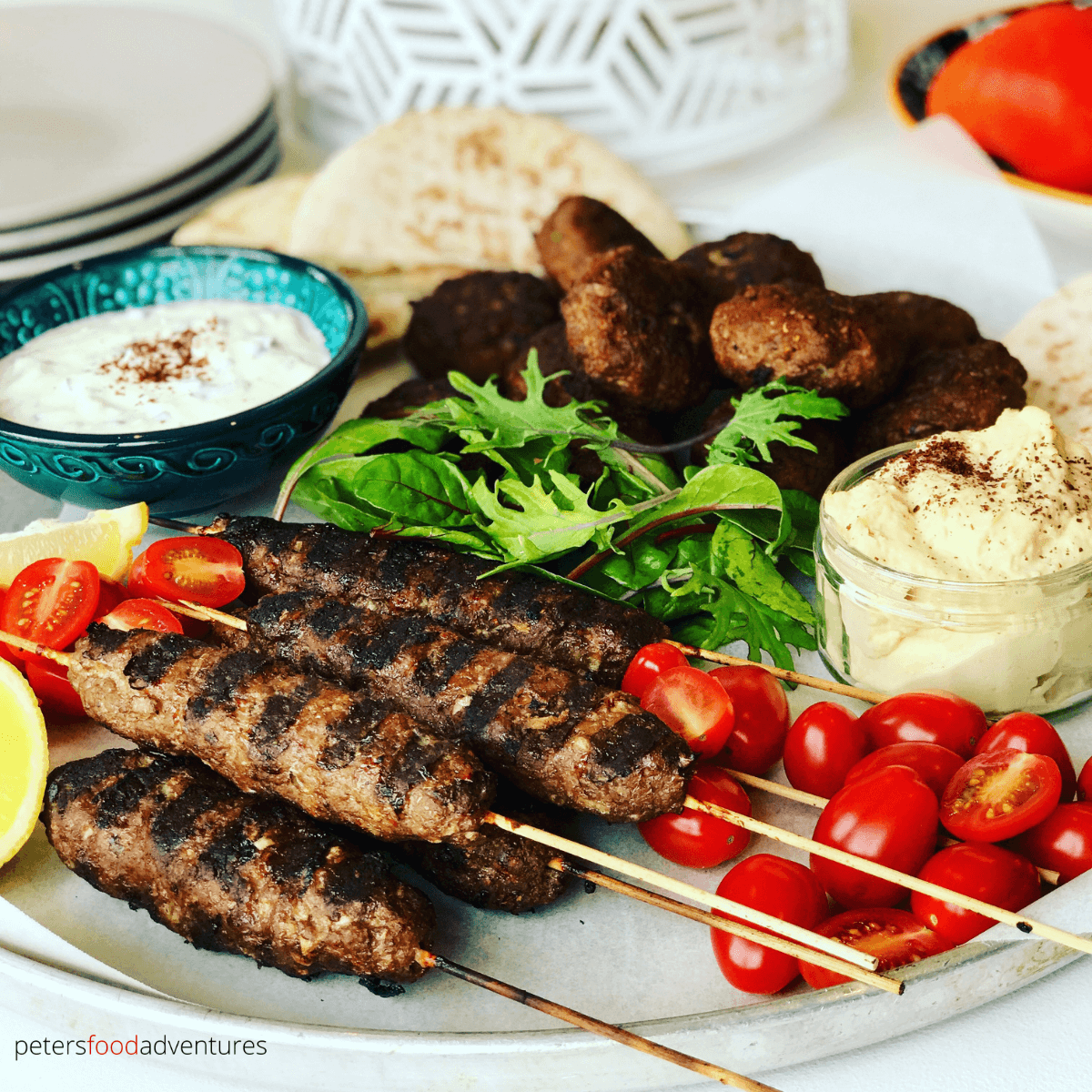 platter of lamb kofta kebabs with hummus, tzatziki, lettuce and plates