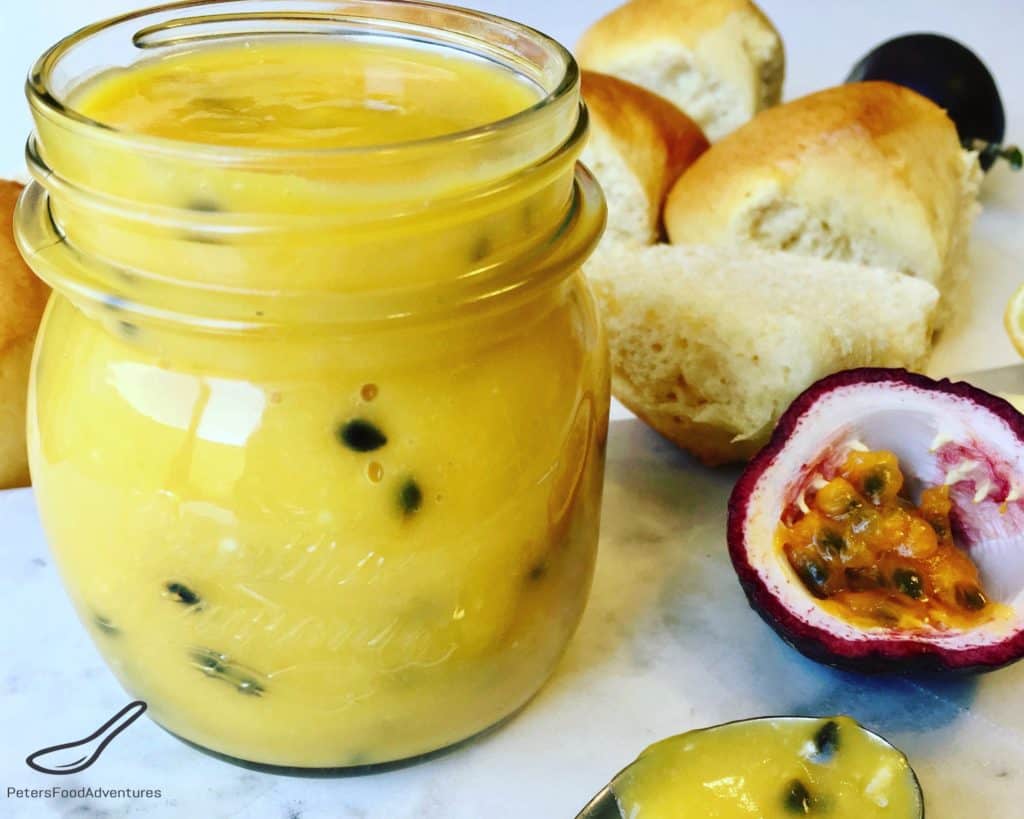 Passionfruit curd in a glass jar, with fresh baked scones beside them