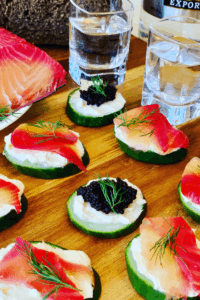 Cucumber Appetizers with caviar and salmon, on a table with 2 shots of vodka