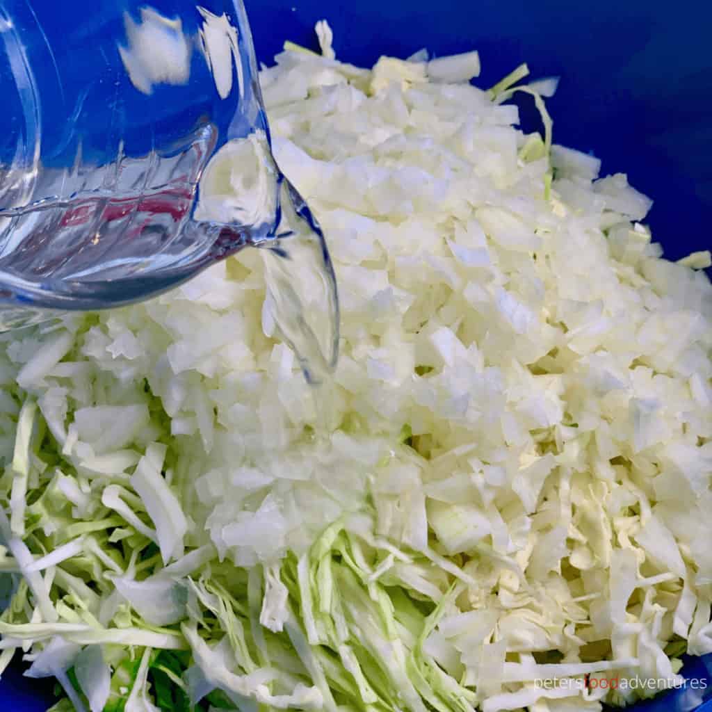 pouring vinegar into sliced cabbage and onion