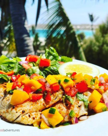 grilled snapper with mango on a plate with palm trees in the background